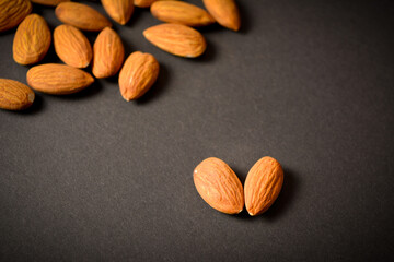 Macro shot of Almond nuts on dark background. One nut in focus. Scattered almonds. Creative food concept. Raw nuts. Copy space image. Single object. Kitchen still life

