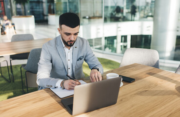 Focused young businessman working on laptop and taking notes