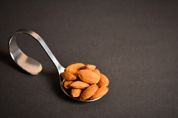 Side view of Almond nuts served on silver metal stainless steel spoon. almonds on dark background. Creative food concept. Raw nuts. Copy space image. Single object. Kitchen still life
