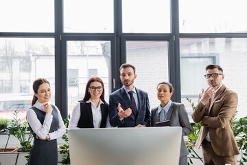 Businessman pointing at computer near cheerful multiethnic colleagues in office