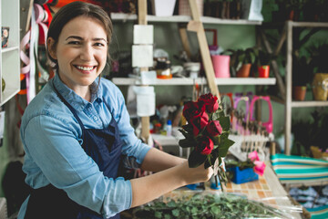 Young adult woman working in city street flower shop.She arranging flowers inside of shop.Small business concept.