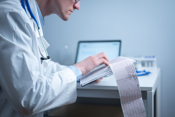 Cardiologist reading an ECG print-out. Doctor analyzing electrocardiogram. Practitioner examine patient test results. Medical and healthcare concept. Physician looking at cardiogram at medical office - obrazy, fototapety, plakaty