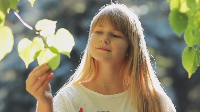 Blonde girl looking at branch with fresh green leaves and smiling outdoor in springtime