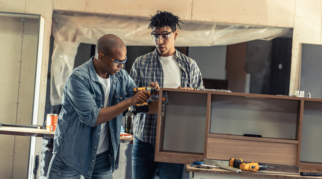 Two young black man carpenter assembling furniture part in they workshop.