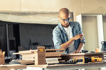 Fototapeta na wymiar Young black man carpenter working in his workshop. He's examining the blueprint and preparing for work. 