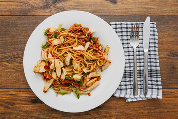 Simple chicken chow mein meal on a white plate and on a wooden table. Chinese style tasty noodles with sauce and vegetables