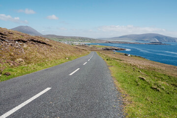 Small narrow road by the ocean, Achill Island, county Mayo, Ireland. Warm sunny day. Irish landscape. Blue clear cloudy sky. Spectacular view