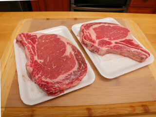 Raw uncooked rib eye steaks in a butcher tray on a wooden cutting board.