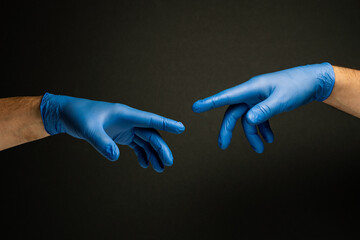 Two hands in medical gloves that reach out to each other resembling Michelangelo's painting of the...
