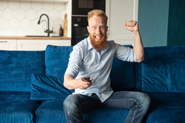Excited smiling young redhead man win in video game and feel happy, a guy with a joystick in hand raising fist in triumph, screams happily