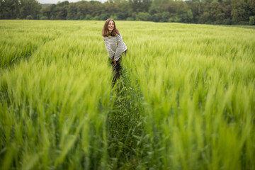 Happy woman walking in green rye field and enjoys calm nature. Freedom and meditation concept. 