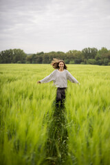 Happy woman walking in green rye field and enjoys calm nature. Freedom and meditation concept. 