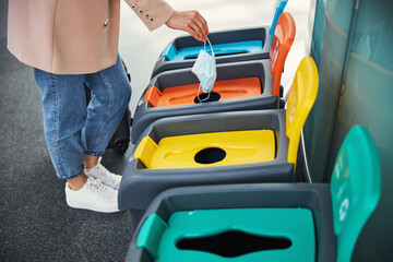 Fototapeta premium Female hand throwing medical mask in trash can at airport