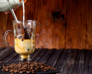 Pouring milk from a bottle to a glass of espresso ice cubes. Cold drink milk with frozen ice cubes .