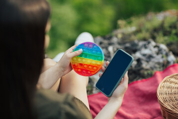 Colourful silicone anti-stress toy pop it and phone in the hands of girl at nature. A new trend for teenagers and children.