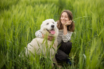 A portrait of happy woman staying in green rye field enjoys calm nature while cute big sheepdog...