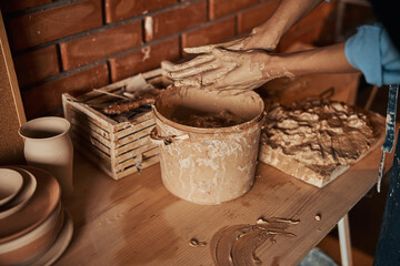 Beautiful elegant craft woman arms shaping something with earthenware ingredient in pottery workshop