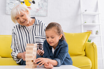 Smiling girl playing blocks wood game near blurred granny