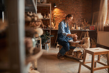 Beautiful brunette ceramicist wearing apron making patterns from fresh wet dirty in art studio