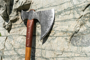 the battle ax is on the ground next to a large stone. forged ax