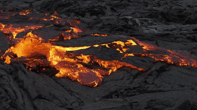 Incandescent lava river flowing slowly through black cooled rocks. Aerial static view