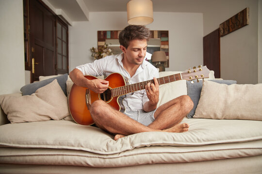 Man playing guitar on sofa at home