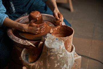 Unrecognized craft woman squeezing earthenware brown mud on pottery wheel in art studio