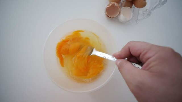 Whisking Egg Yolks With Fork In Bowl Top View With Broken Egg Shells In Background
