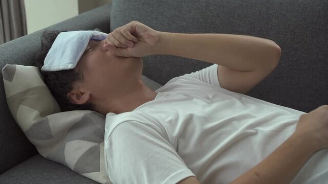 Sick Asian young man got a flu or influenza virus and resting on a sofa.