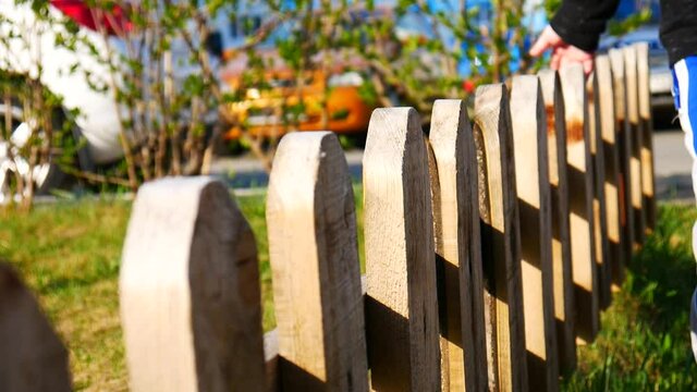 Close-up of a wooden fence and a boy walking and running his hand along it