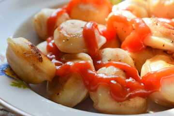 Close-up and selective focus of fried juicy dumplings drizzled with ketchup. Traditional Russian home-made food. Dumplings, ravioli with meat.
