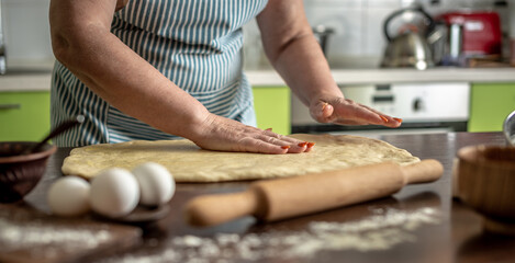 Woman at home in her kitchen is gently laying out the dough for cooking homemade fragrant homemade pastries