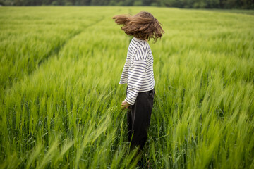Happy woman walking in green rye field and enjoys calm nature. Freedom and meditation concept. 