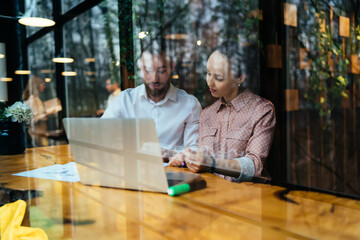 Concentrated male and female employee working with laptop and documents