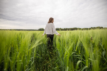 Happy woman walking in green rye field and enjoys calm nature. Freedom and meditation concept. 