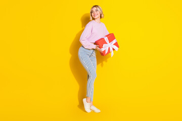 Full length photo of happy positive dreamy young woman look empty space hold present isolated on yellow color background