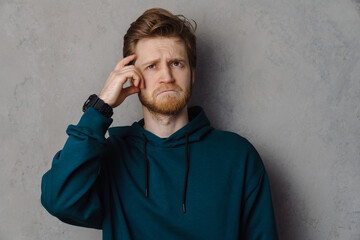 Bearded ginger man wearing wristwatch frowning and looking upward