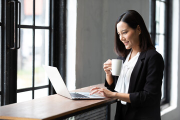 businesswoman working with laptop computer and holding a cup of coffee in office