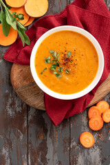 Creamy sweet potato soup with carrots and spices in a white bowl on a dark background top view. Tasty vegan sweet potato soup, autumn food.