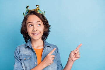 Photo of young preteen boy happy positive smile crown prince point finger empty space ad choice isolated over blue color background