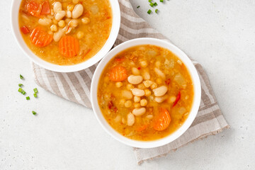 Soup with beans and vegetables in a bowl on a gray concrete background top view. Soup made from lentils, chickpeas, white beans, carrots, peppers, and tomatoes. Tasty vegan soup, vegetarian food.