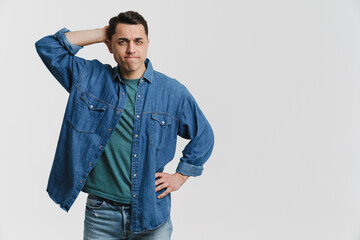 Young brunette man dressed denim shirt frowning and holding his head