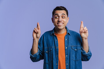 Young brunette man smiling and holding fingers crossed