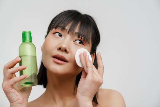 Young Asian Shirtless Woman Cleaning Her Face With Lotion