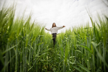 Happy woman staying with raised hands in green rye field and enjoys calm nature. Freedom and...