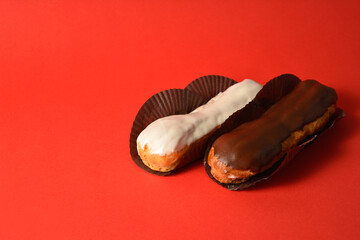 Classic French desserts. Eclairs with white and dark chocolate filled with custard cream served on dessert paper pieces. Two Puffy Eclairs on red background. Choux pastry. Copy space image
