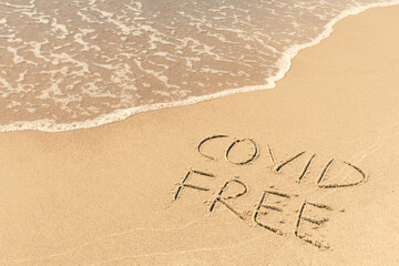 Covid free written on the shore, on the sand of a beach with wave washing the word, erasing or canceling it during Coronavirus summer, Covid free, safe beach, vaccine. Covid-19 immunity passport, pass