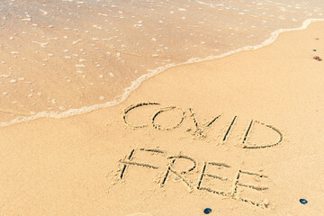 Covid free written on the shore, on the sand of a beach with wave washing the word, erasing or canceling it during Coronavirus summer, Covid free, safe beach, vaccine. Covid-19 immunity passport, pass