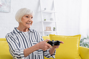 KYIV, UKRAINE - JANUARY 11, 2021: Elderly woman in casual clothes playing video game on blurred joystick