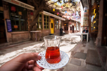 Glass of tea in hand of a visitor of outdoor cafe in a Turkish town. Dinner on street it traditional way in Turkey